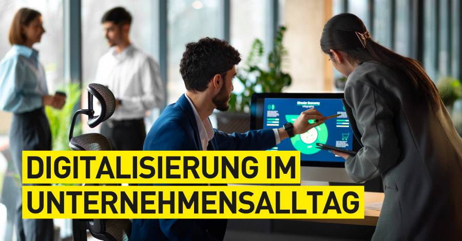 Zwei Personen besprechen digitale Daten am Bildschirm, im Hintergrund weitere Kollegen