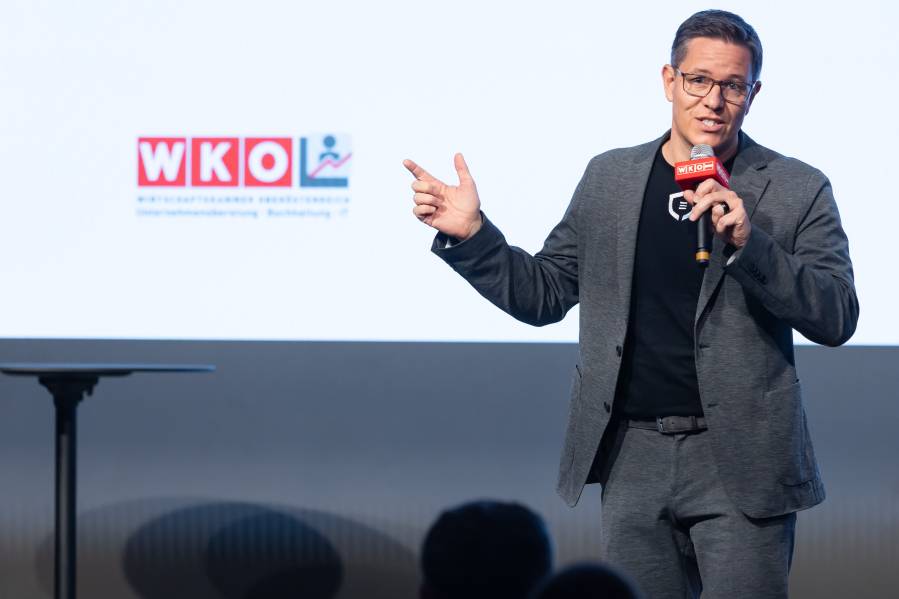 Vortragender mit WKO-Mikrofon auf einer Bühne vor WKO-Logo.