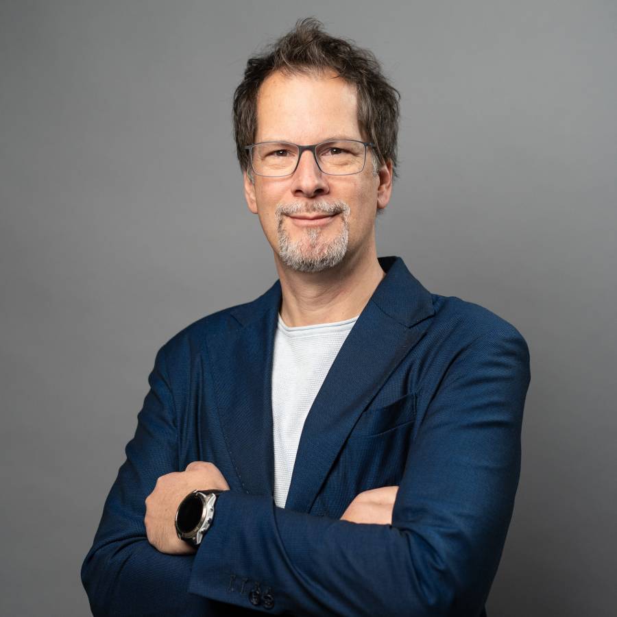 Elmar Jilka, IT-Experte, steht in blauem Anzug vor grauem Hintergrund