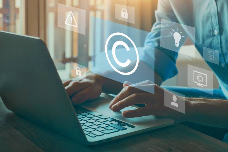 Person tippt auf Laptop, eingeblendetes Copyright-Symbol und Sicherheitssymbole.